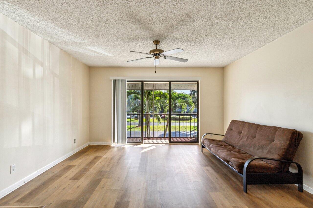 A living room with wood-look flooring, a brown futon, and a sliding glass door — 618 Sea Pine Way # A2, FL 33415, FL