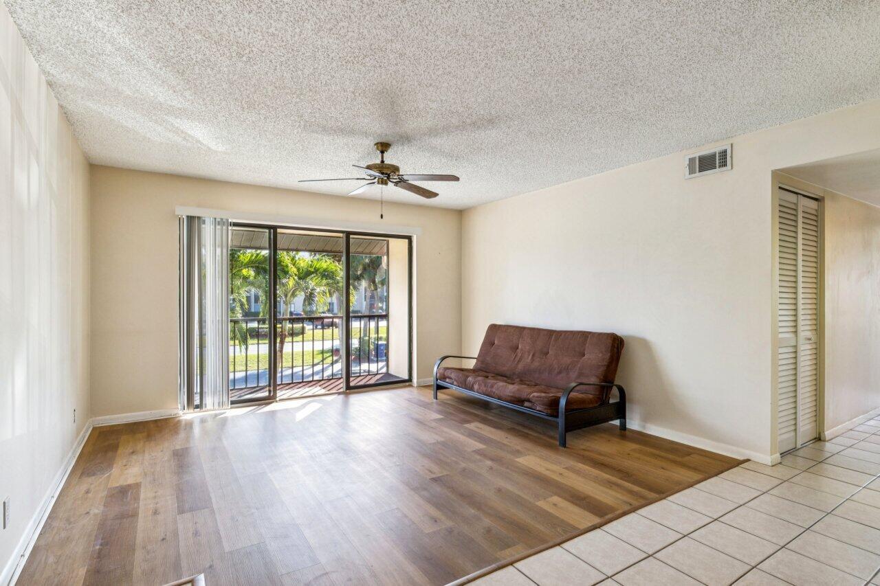 A living room features wood-look flooring, a brown futon, a ceiling fan, and sliding glass doors — 618 Sea Pine Way # A2, FL 33415, FL