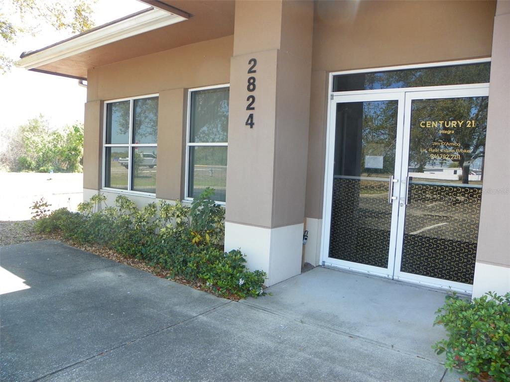 The exterior of a commercial building features a glass entrance door and address numbers — 2824 MANATEE AVENUE E, BRADENTON, FL