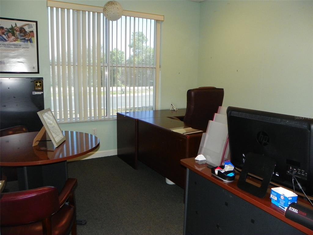 An office features a dark wood desk, a round meeting table, and vertical window blinds — 2824 MANATEE AVENUE E, BRADENTON, FL