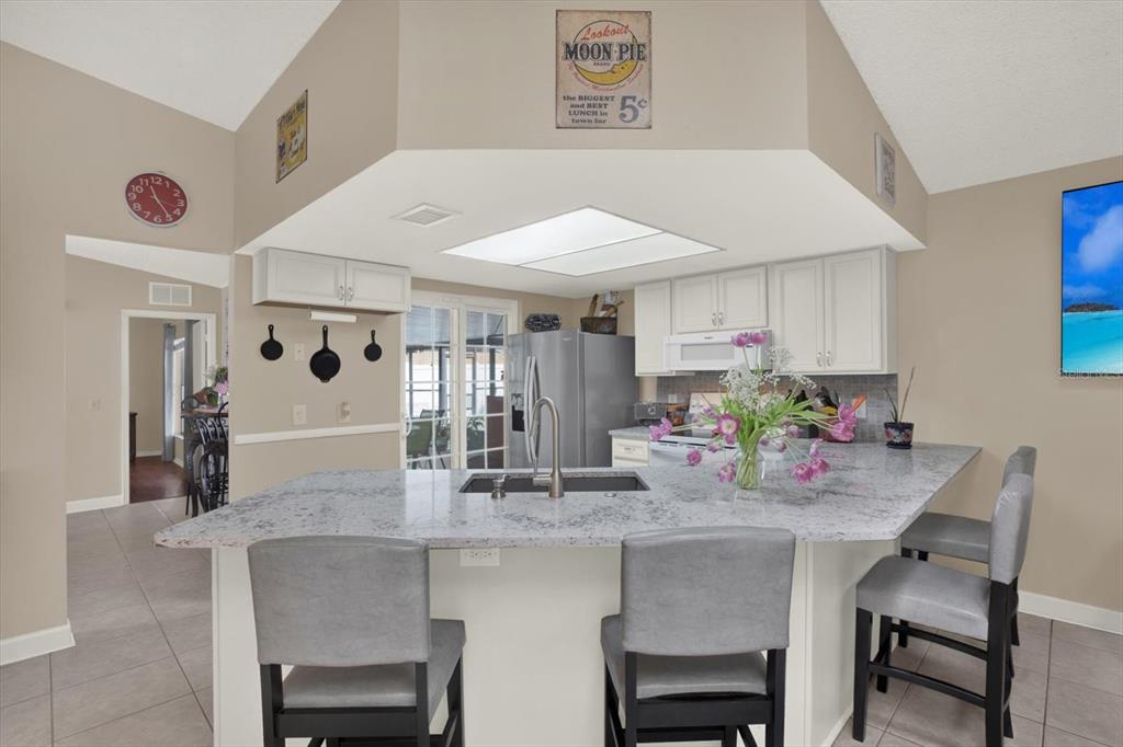 A kitchen features a large granite island with bar seating, white cabinets, and stainless appliances — 729 SANDY CREEK DRIVE, BRANDON, FL