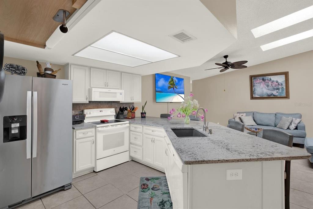 A kitchen with white cabinets, granite countertops, and a large island opens to a living area — 729 SANDY CREEK DRIVE, BRANDON, FL