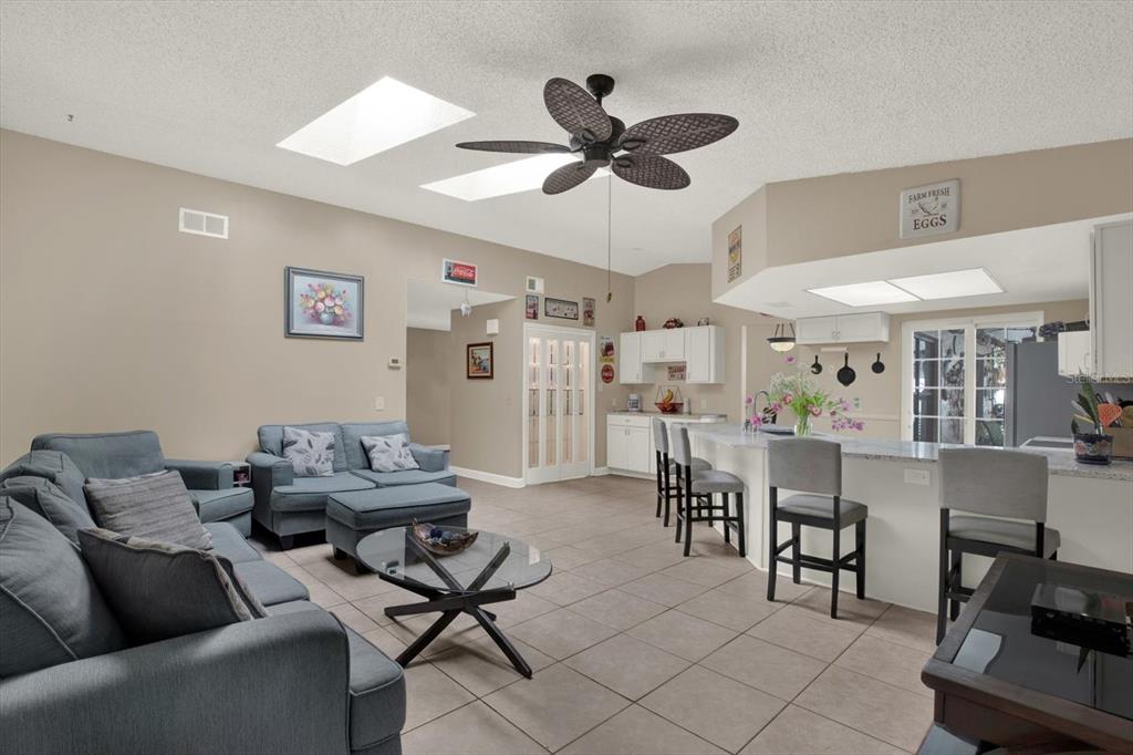 A living room with tile floors, a ceiling fan, and an open kitchen with bar seating — 729 SANDY CREEK DRIVE, BRANDON, FL