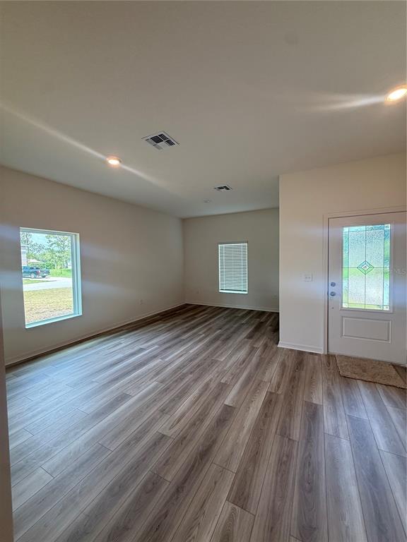 An empty room features light-colored walls, wood-look flooring, two windows, and a front entry door — 2921 GARRET STREET, DELTONA, FL