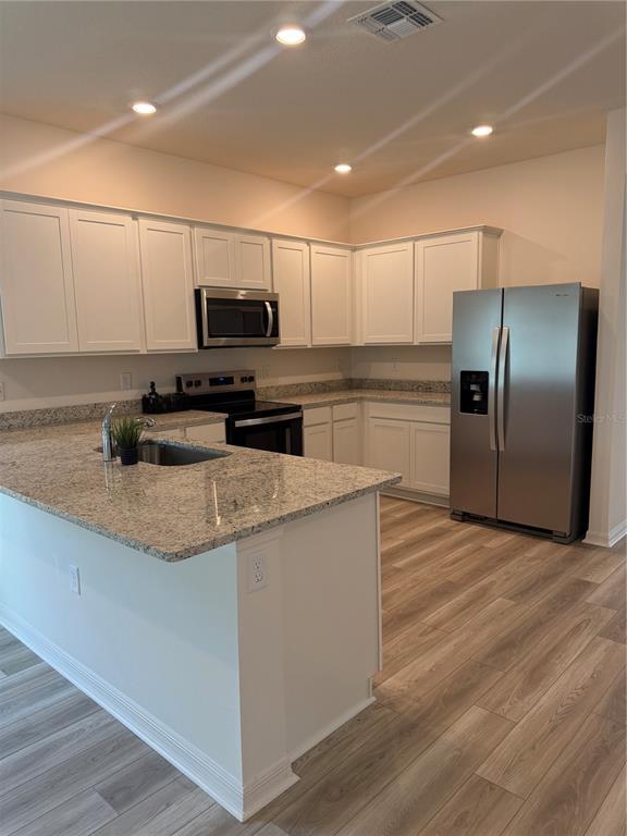 A kitchen with white cabinets, granite countertops, stainless steel appliances, and wood-look flooring — 2921 GARRET STREET, DELTONA, FL