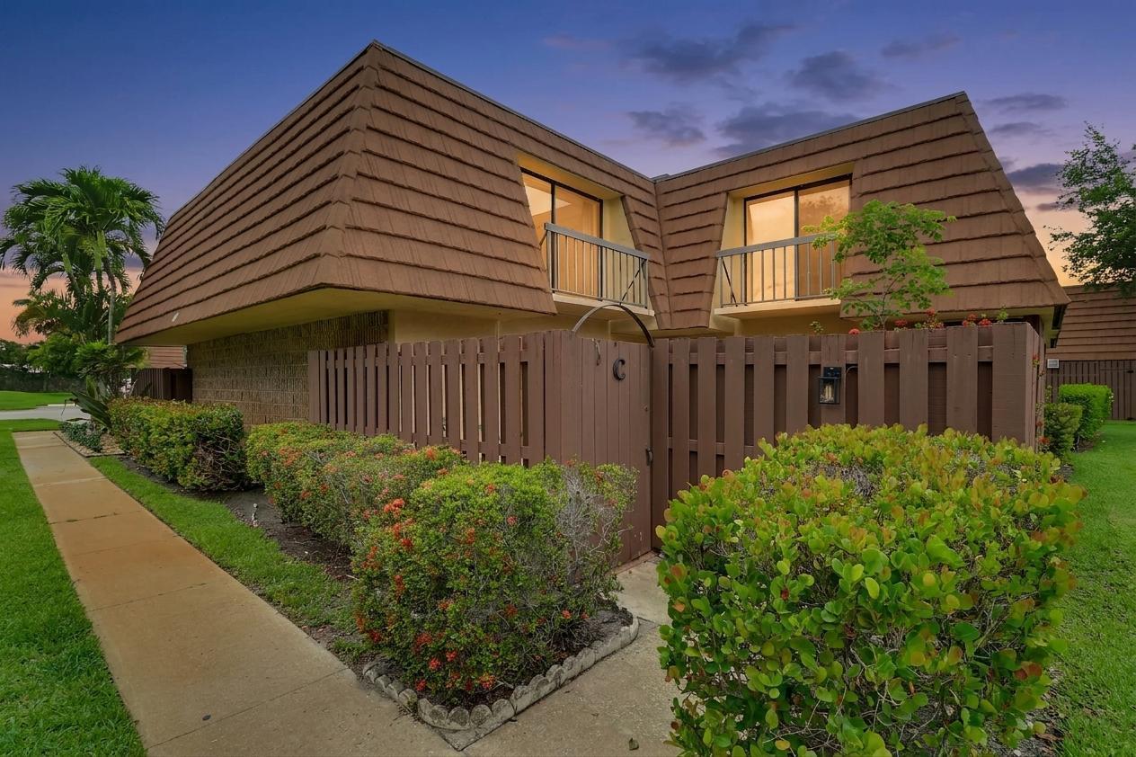 A two-story townhouse exterior with a brown mansard roof, private fenced courtyard, and balcony — 825 Center Street # 49c, Jupiter FL 33458, JUPITER, FL