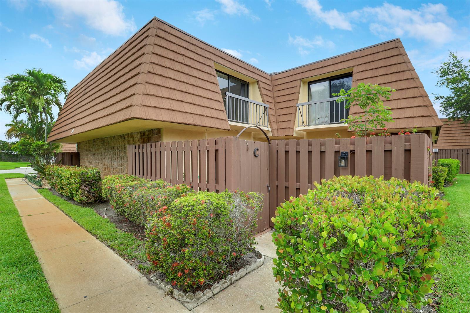 A two-story townhouse with a brown mansard roof, a wooden privacy fence, and landscaped bushes — 825 Center Street # 49c, Jupiter FL 33458, JUPITER, FL