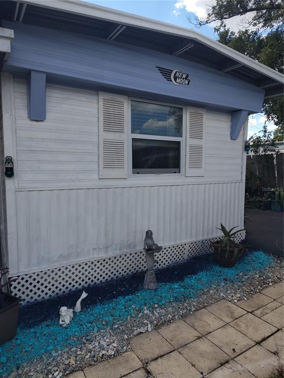 The exterior of a mobile home features white siding, a blue accent panel, and decorative landscaping — 37748 MARKLAND AVENUE, ZEPHYRHILLS, FL