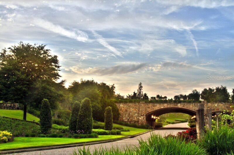 A stone bridge arches over a paved driveway surrounded by landscaped lawns and trees — 16122 TRIVOLI CIRCLE, BELLA COLLINA, FL
