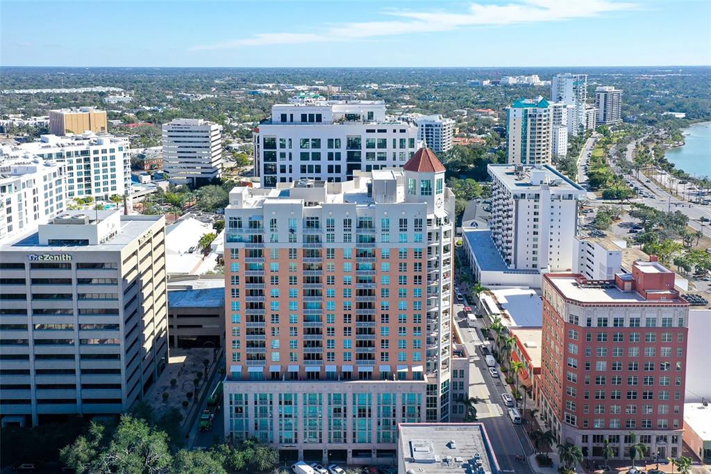 An aerial view shows a tall, peach-colored residential building surrounded by other urban high-rises — 1350 MAIN STREET UNIT 1007, SARASOTA, FL