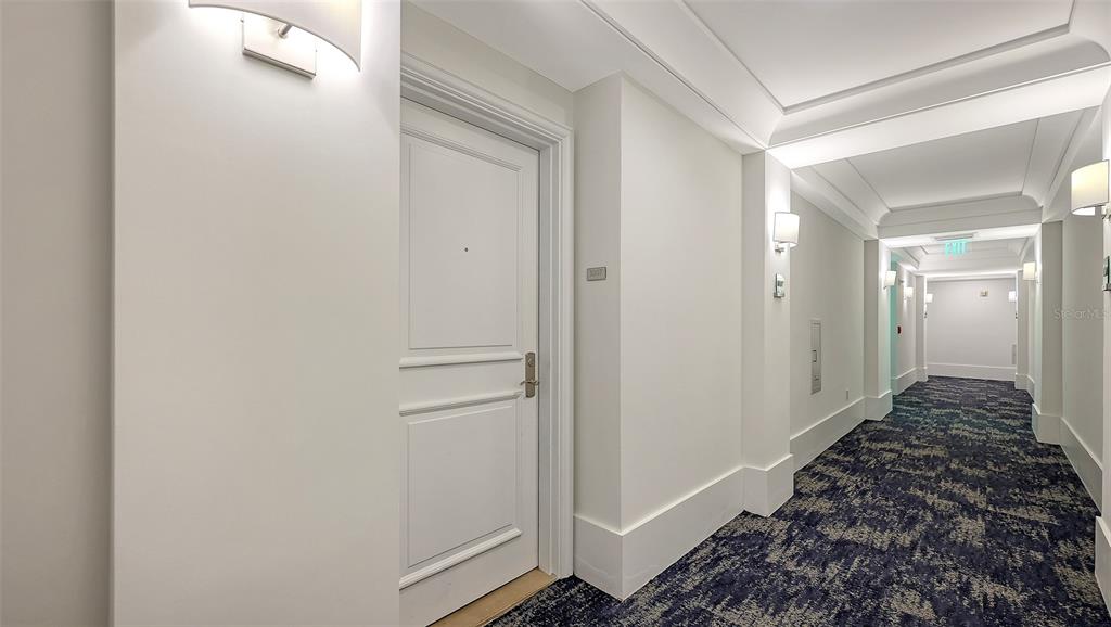 A white door leads into a hallway with patterned blue carpet and recessed ceiling lighting — 1350 MAIN STREET UNIT 1007, SARASOTA, FL
