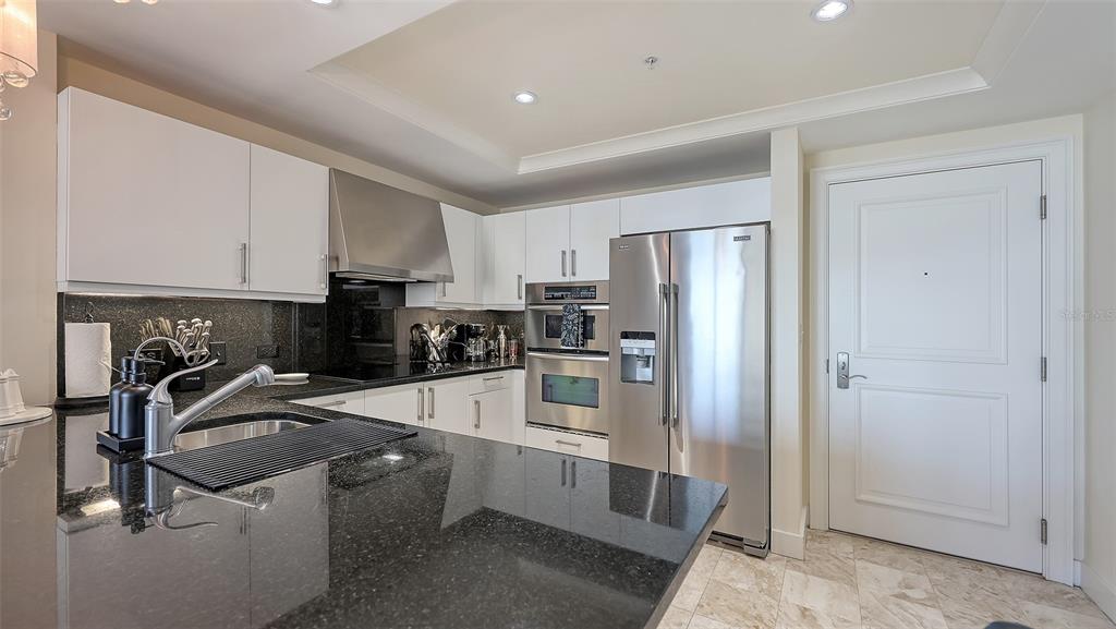 A modern kitchen features white cabinetry, black granite countertops, and stainless steel appliances — 1350 MAIN STREET UNIT 1007, SARASOTA, FL