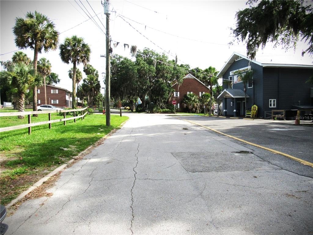 A paved road leads toward a brick building and a dark-sided structure with palm trees — 14 S LAKE STREET, CRESCENT CITY, FL