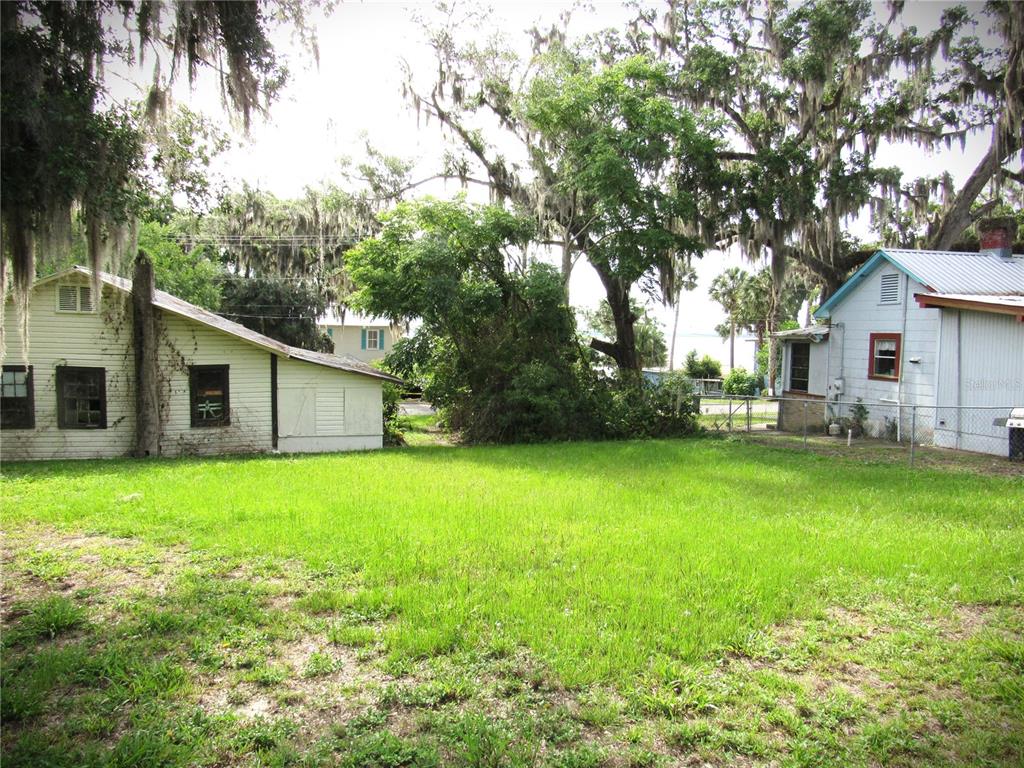 A grassy yard sits between two small, light-colored houses under large, moss-covered trees — 14 S LAKE STREET, CRESCENT CITY, FL