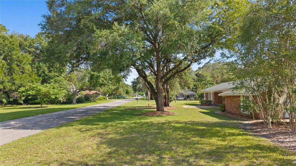 A brick house sits on a grassy lot shaded by large trees along a street — 214 SE 2ND STREET, CHIEFLAND, FL