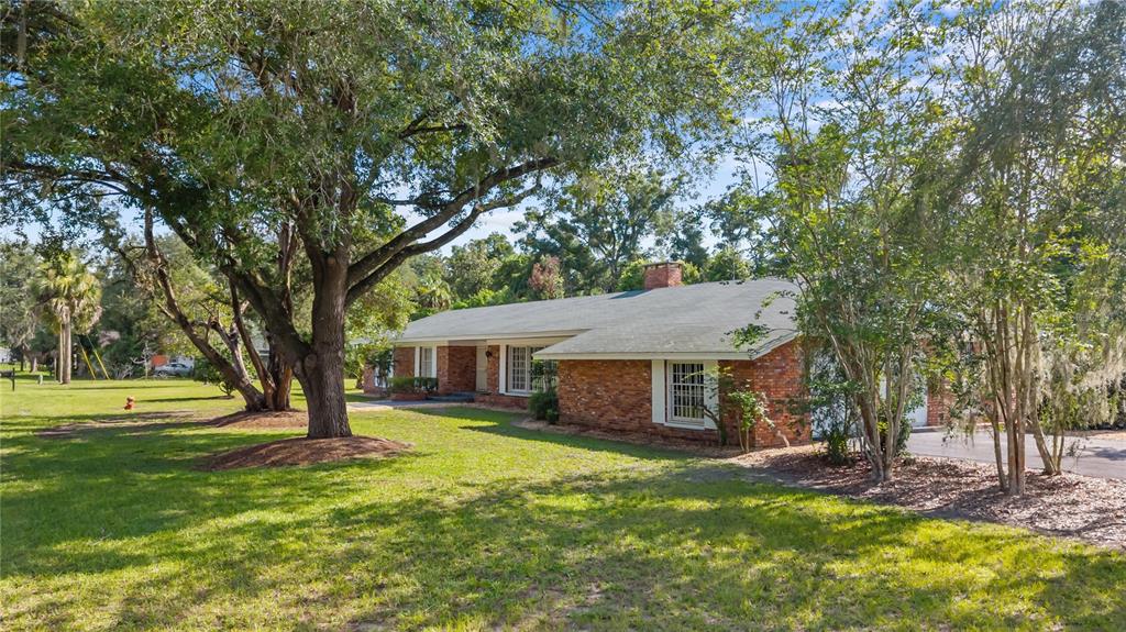 A single-story brick house with a gray roof sits on a grassy lot with trees — 214 SE 2ND STREET, CHIEFLAND, FL