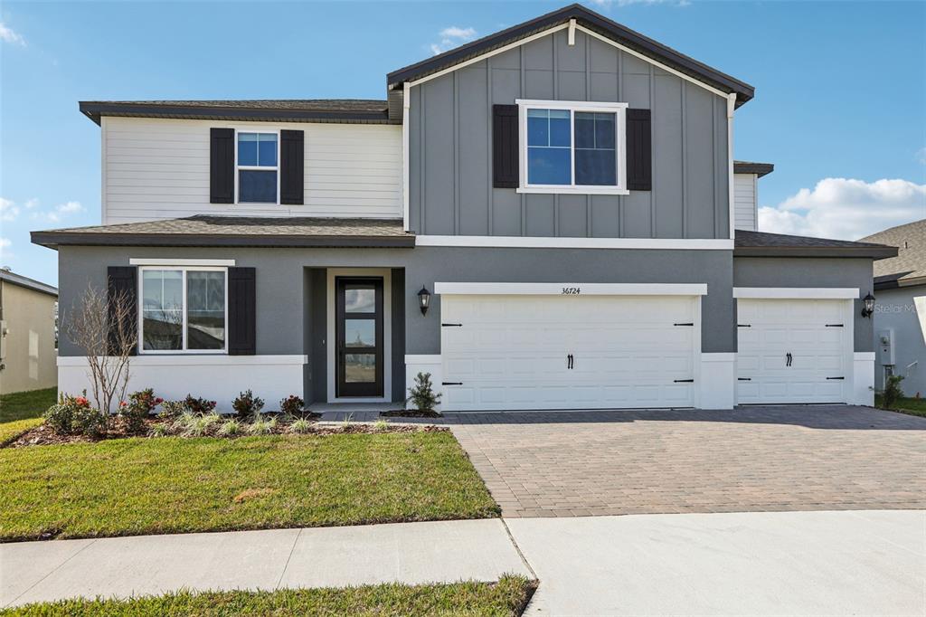 A two-story house features a gray and white exterior with a three-car garage — 36724 MELSTONE WAY, ZEPHYRHILLS, FL