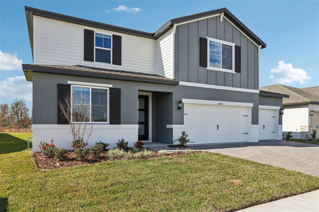 A two-story house with gray and white siding, a three-car garage, and a front lawn — 36724 MELSTONE WAY, ZEPHYRHILLS, FL
