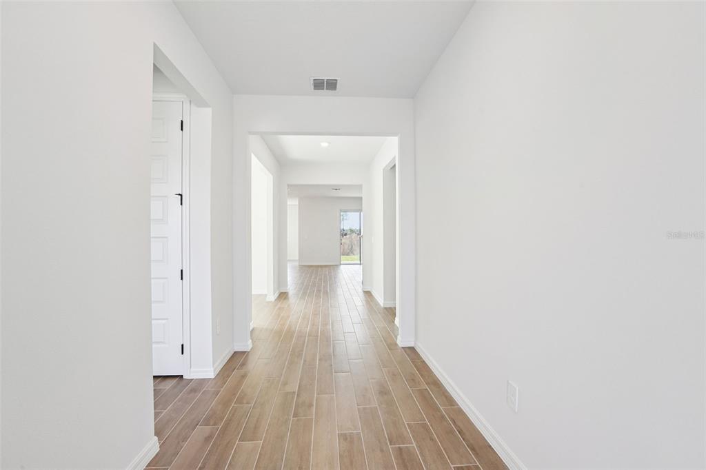 A bright hallway with light wood-look tile flooring leads toward an open living area — 36724 MELSTONE WAY, ZEPHYRHILLS, FL