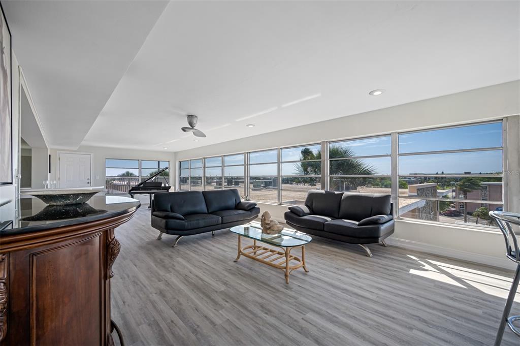 A living room with light wood floors, two black sofas, a glass coffee table, and windows — 6363 GULF WINDS DRIVE UNIT 437, ST PETE BEACH, FL