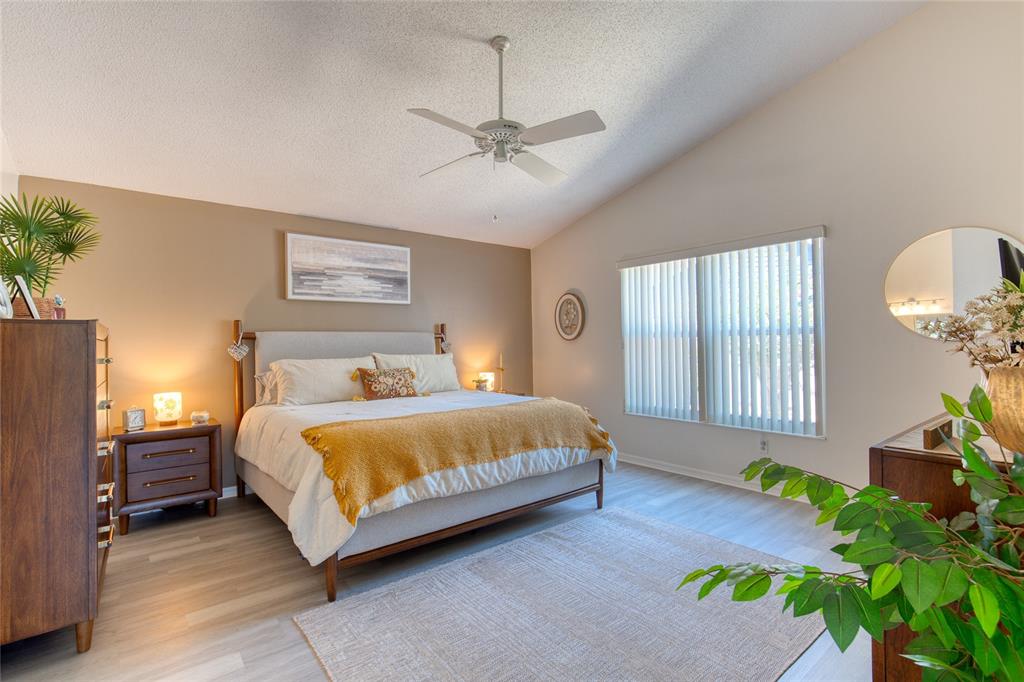 A bedroom features a bed with a yellow throw, a ceiling fan, and light flooring — 982 BREEZEMONT COURT, PORT ORANGE, FL