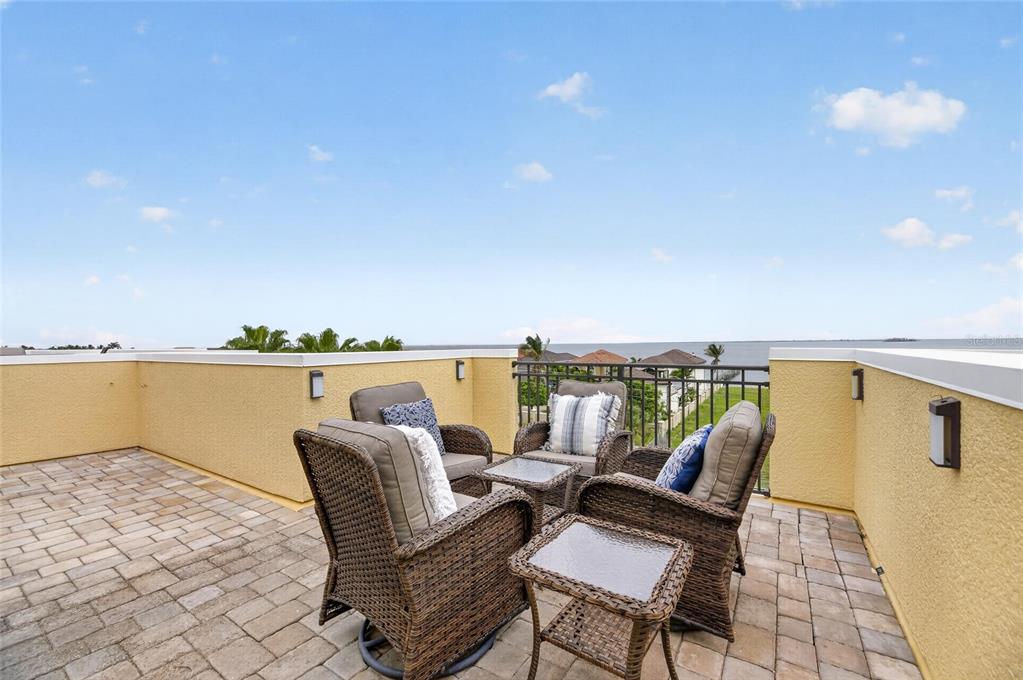 A rooftop patio features wicker furniture and pavers overlooking a body of water — 6408 MAYRA SHORES LANE, APOLLO BEACH, FL