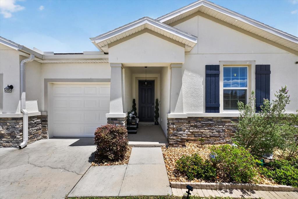 The exterior of a single-story house features a garage, stone veneer, and a covered entryway — 13504 GOLDEN LIME AVENUE, SPRING HILL, FL