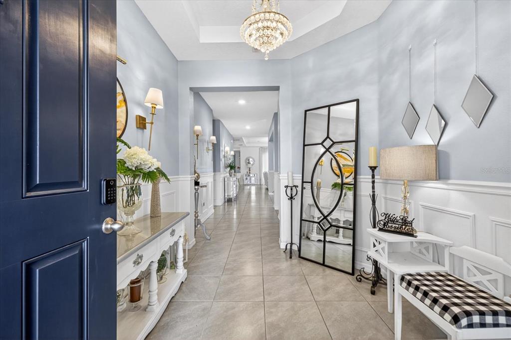 A bright foyer features light blue walls, tile flooring, a crystal chandelier, and a console table — 13504 GOLDEN LIME AVENUE, SPRING HILL, FL
