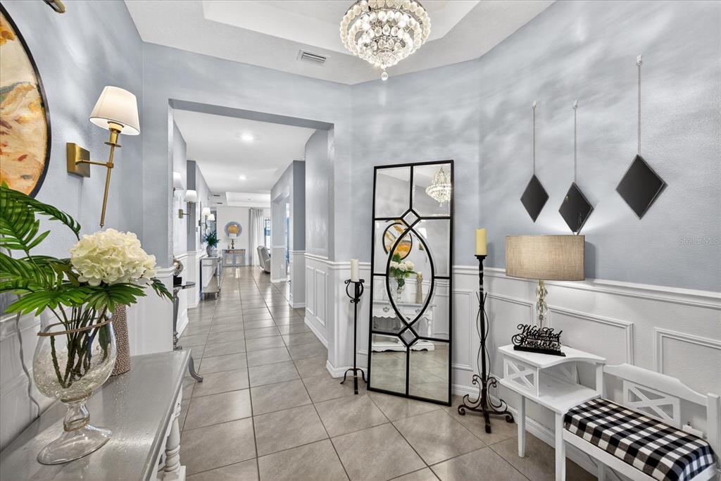 A bright foyer features a crystal chandelier, a large floor mirror, and a long hallway — 13504 GOLDEN LIME AVENUE, SPRING HILL, FL