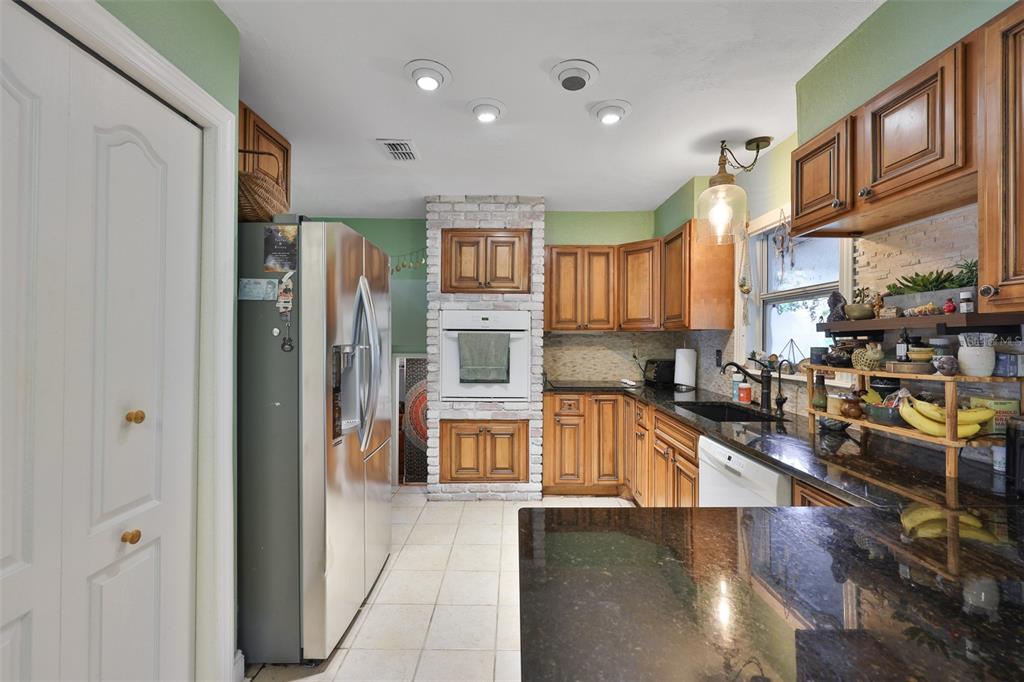 A kitchen features wood cabinets, dark granite countertops, a brick-encased wall oven, and green walls — 401 OVERLAND DRIVE, BRANDON, FL