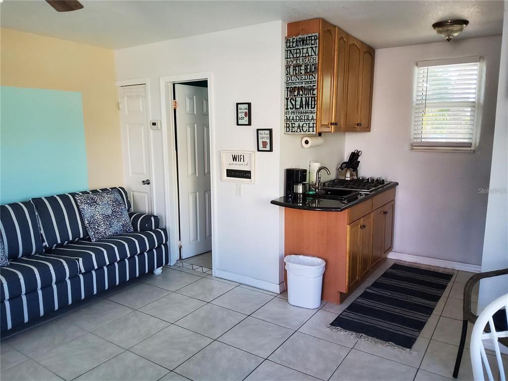 A small kitchenette with wooden cabinets and a striped sofa in a tiled room — 603 MANDALAY AVENUE UNIT 212, CLEARWATER, FL