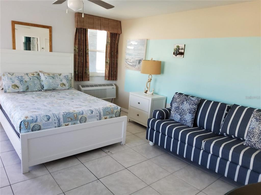 A bedroom features a white bed, a striped sofa, a nightstand, and tile flooring — 603 MANDALAY AVENUE UNIT 212, CLEARWATER, FL
