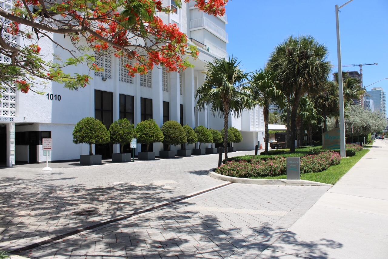 The exterior of a white building features a paved driveway, manicured trees, and palm trees — 1010 S Ocean Boulevard # 1214, Pompano Beach FL 33062, POMPANO BEACH, FL
