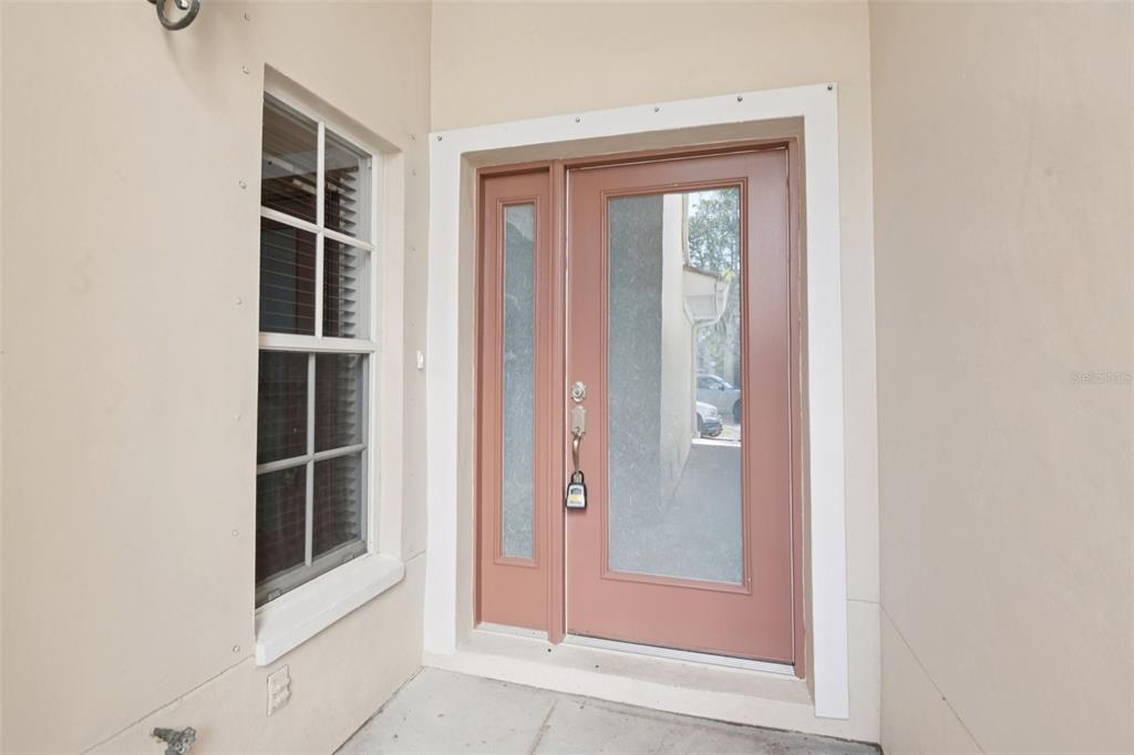 A pink front door with a glass sidelight sits next to a window on a porch — 300 VALENCIA CIRCLE, ST PETERSBURG, FL