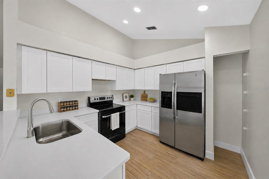 A kitchen features white cabinets, stainless steel appliances, quartz countertops, and light wood-look flooring — 2007 59TH CIRCLE S, ST PETERSBURG, FL