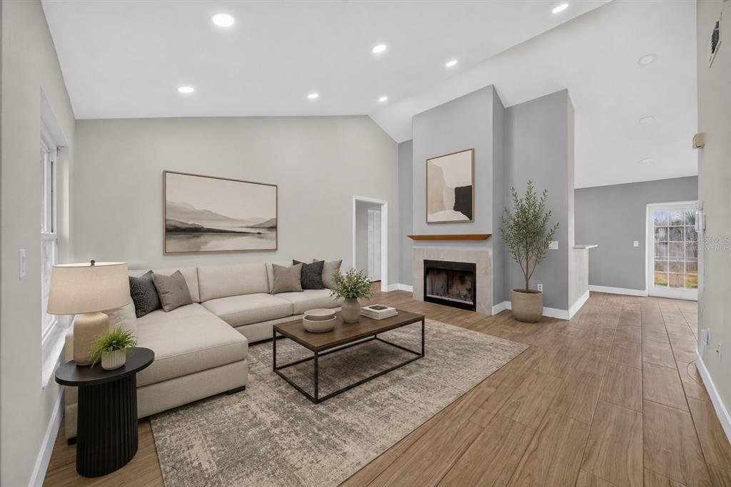 A living room with a sectional sofa, fireplace, and wood-look tile flooring under vaulted ceilings — 2007 59TH CIRCLE S, ST PETERSBURG, FL