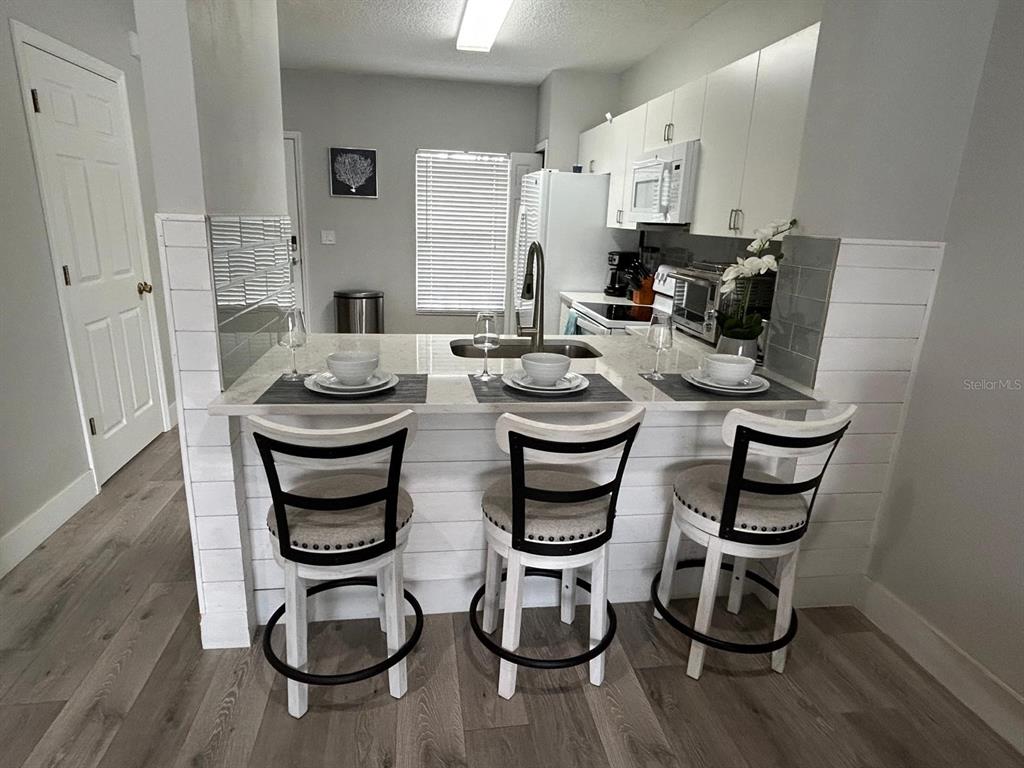 A kitchen features a breakfast bar with three stools, white cabinetry, and wood-look flooring — 4629 SABAL KEY DRIVE UNIT 4629, BRADENTON, FL