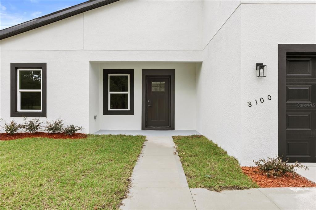 The exterior of a white house features a dark front door, windows, and garage door — 8100 N TINY LILY DRIVE, CITRUS SPRINGS, FL