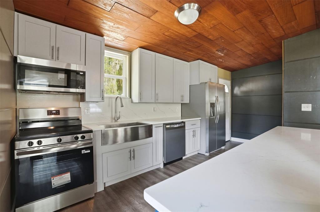 A kitchen features light gray cabinets, stainless steel appliances, a farmhouse sink, and wood-paneled ceilings — 320 S OTIS AVENUE, LECANTO, FL