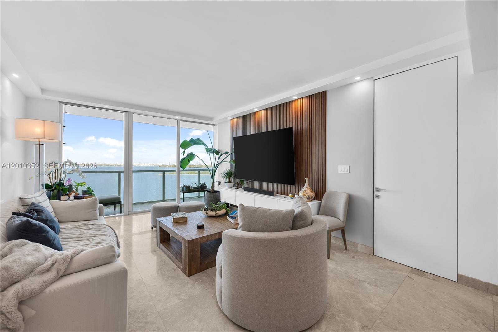 A modern living room features a wood-slatted accent wall, a large television, and balcony views — 665 NE 25th St # 1503, Miami FL 33137, MIAMI, FL