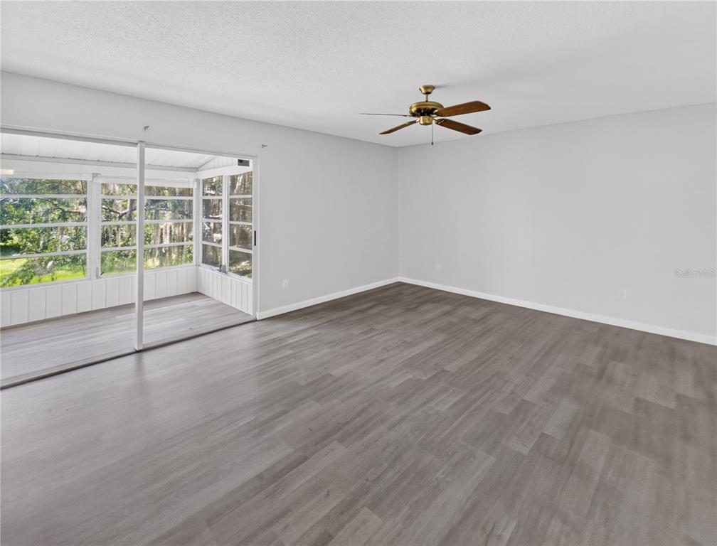 An empty room with gray wood-look flooring, a ceiling fan, and sliding doors to a porch — 600 FAIRWAYS CIRCLE UNIT B, OCALA, FL