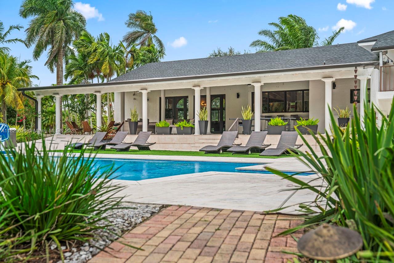 A swimming pool with lounge chairs sits in front of a house with a covered patio — 14875 SW 212th St, Miami FL 33187, MIAMI, FL