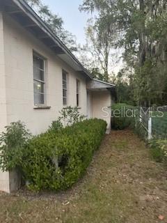 A side view of a light-colored concrete block house with a hedge and trees — 1235 SAGE STREET, MONTICELLO, FL