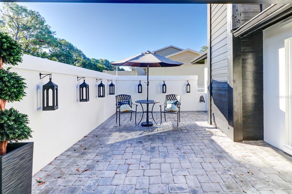 A paved patio features a small bistro set under an umbrella against a white wall — 16212 W COURSE DRIVE, TAMPA, FL