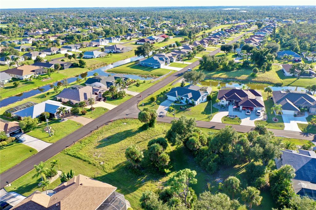An aerial view shows a suburban neighborhood with houses, green lawns, and a winding canal — 2 SPORTSMAN WAY, ROTONDA WEST, FL