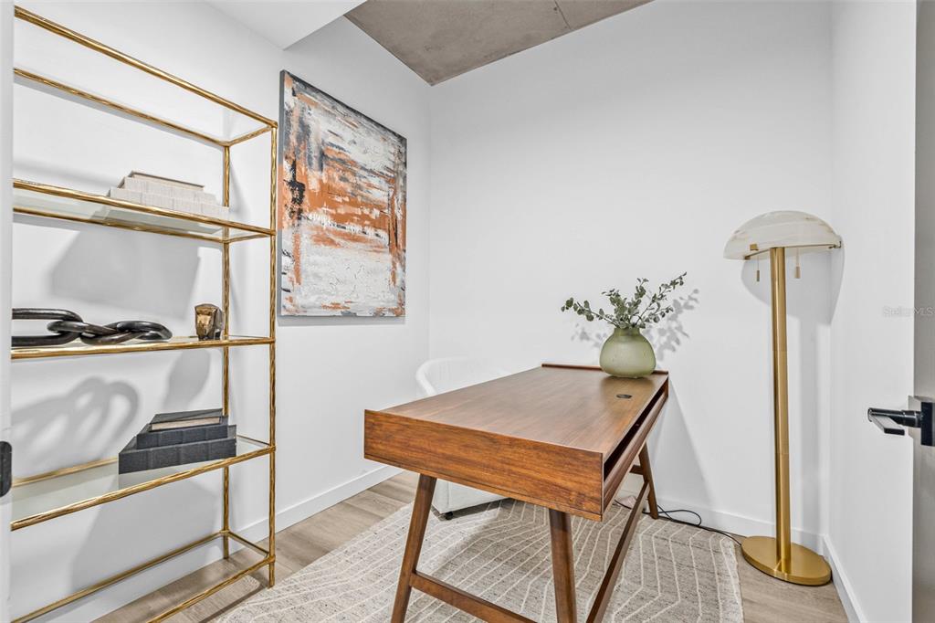 A small home office features a wooden desk, gold shelving, a floor lamp, and abstract art — 221 MAIN STREET N UNIT B3-716, ST PETERSBURG, FL