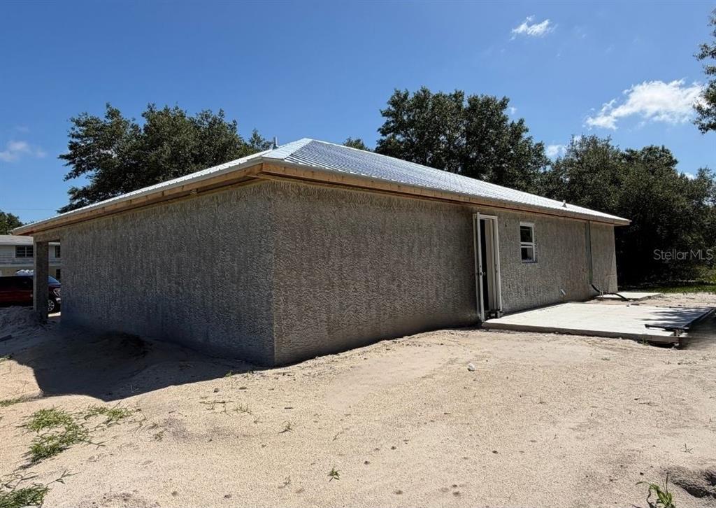 A side view of a house with a stucco exterior, metal roof, and concrete patio — 8115 SW EASY STREET, ARCADIA, FL