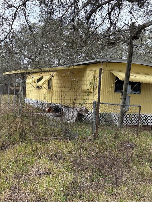 A yellow mobile home with metal awnings sits behind a chain-link fence — 12013 BETHWOOD AVENUE, NEW PORT RICHEY, FL