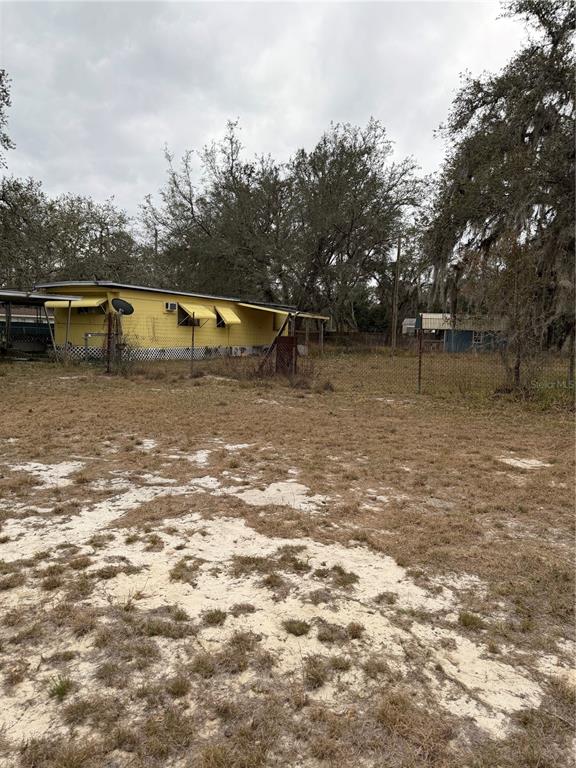 A yellow mobile home sits on a sandy, fenced lot with mature trees — 12013 BETHWOOD AVENUE, NEW PORT RICHEY, FL