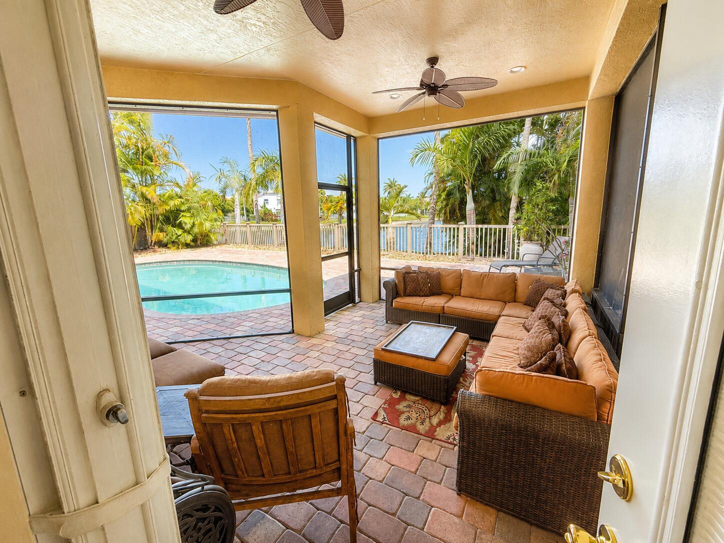 A screened-in patio features a brick floor, wicker sectional seating, and a view of a pool — 3008 Hamblin Way, Wellington FL 33414, WELLINGTON, FL